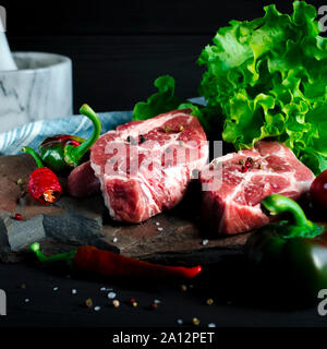 Due bistecche sugose giacciono su una pietra selvatici accanto al rosso e peperoncini verdi e una fresca insalata verde su un tavoli in legno nero Foto Stock