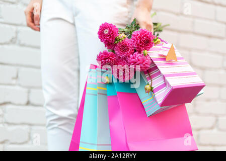 Fiori di colore rosa nel femminile la mano e borse per lo shopping su sfondo mattone. Compleanno, madre, Donna giorno di nozze concetto. Mazzetto di carta buste regalo. Foto Stock