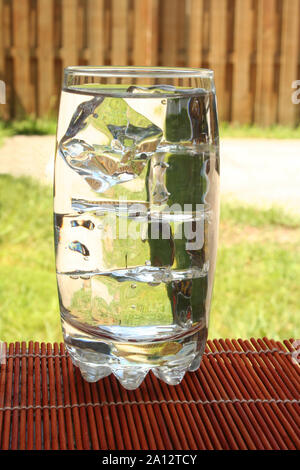 Bicchiere grande di acqua dolce su un tappetino in legno all'esterno. Foto Stock