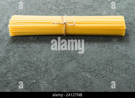 Materie spaghetti legato con una corda su una texture nera dello sfondo. Copia dello spazio. Foto Stock