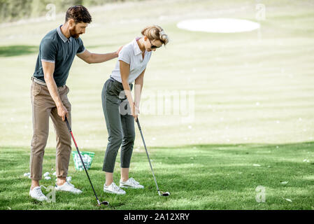 Maschio insegnamento istruttore giovane donna per giocare a golf sul campo da golf in una giornata di sole Foto Stock