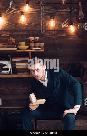 Educazione sostenibile concetto. Ragazzo con stile con capelli e barba la lettura di un libro. Gentleman in vacanza in cottage di legno. Foto Stock