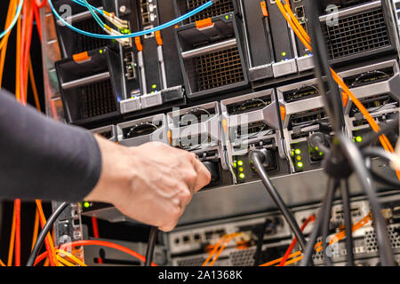 Tecnico di sesso maschile che collega il cavo di alimentazione al cluster di server blade nel data center Foto Stock