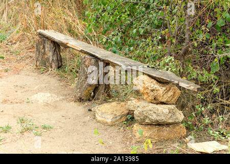 Un vecchio banco di legno verde, boccole, alberi, erba secca, in ucraino giardino di roccia. Foto Stock
