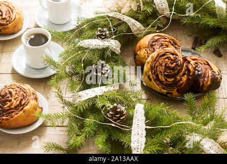 Lumaca muffin al cioccolato servito con il caffè sullo sfondo di una ghirlanda di rami di abete e coni. Stile rustico. Foto Stock