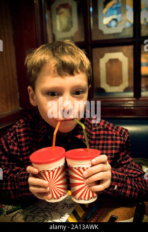 Vista di un ragazzo sorseggiando un drink da due bicchieri. Foto Stock