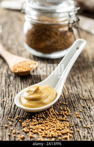 Giallo senape in ceramica e cucchiaio di semi di senape sul vecchio tavolo in legno. Foto Stock