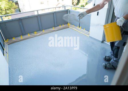 Un lavoratore edile rinnova il balcone piano e chip si diffonde la copertura del pavimento e su resina e rivestimento di colla prima applaying sigillante per acqua Foto Stock