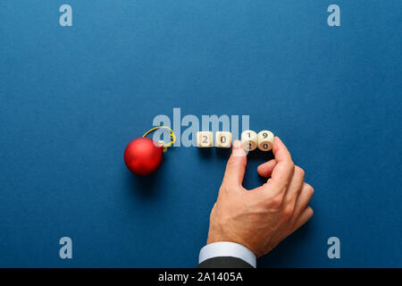 Vacanza rosso ninnolo accanto a un 2019 segno su plinti in legno con maschio girando a mano le ultime due dadi per cambiare la data nel 20120. Su blu navy backgroun Foto Stock