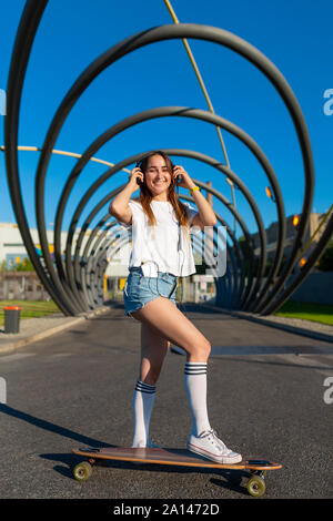 Ragazza adolescente ride su logboard e ascolto di musica dalle cuffie. Foto Stock