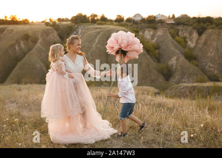 Elegante ragazzo dà un grande fiore a sua madre in un campo al tramonto. Foto Stock