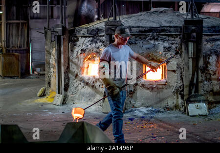 27 sett 2019 Kokomo Indiana USA; un lavoratore svolge un mestolo di acqua calda, il vetro fuso da un forno caldo, per aggiungere a una macchina che verrà poi trasformarlo in un Foto Stock