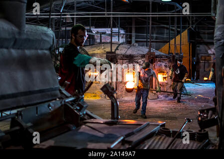 27 sett 2019 Kokomo Indiana America; i lavoratori in una fabbrica di vetro, rapidamente portare il crogiolo siviere riempito con acqua calda, vetro fuso ad una macchina dove un altro w Foto Stock