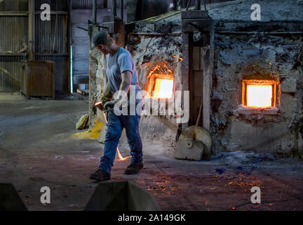 27 sett 2019 Kokomo Indiana USA; un lavoratore svolge un mestolo di vetro fuso, appena rimosso da un molto caldo in forno a una fonderia in America del Nord Foto Stock