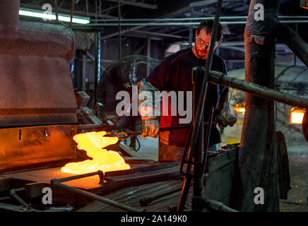 27 sett 2019 Kokomo Indiana USA; questo lavoratore di vetro è la miscelazione allo stato fuso di vetro caldo, che sarà presto trasformato in vetro macchiato fogli. sebbene difficili Foto Stock