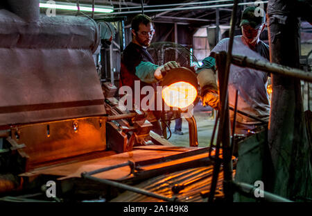 27 sett 2019 Kokomo Indiana America; i lavoratori in una fabbrica di vetro utilizzare mestoli in fusione di vetro caldo, per versare su di una macchina che sarà il roll out fogli di beau Foto Stock