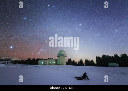 Un stargazer siede nella neve per visualizzare la Via Lattea invernale e luce zodiacale in Nanshan osservatorio. Foto Stock