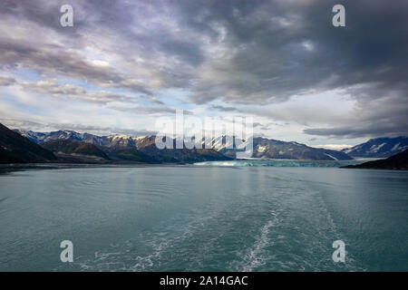 La scia di una nave da crociera vela lontano dal ghiacciaio Hubbard con una vista del ghiacciaio e le montagne. Foto Stock