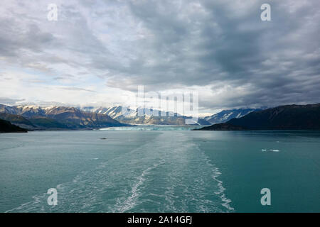 La scia di una nave da crociera vela lontano dal ghiacciaio Hubbard con una vista del ghiacciaio e le montagne. Foto Stock