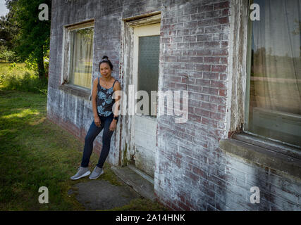 Donna asiatica in jeans e scarpe da ginnastica in piedi di fronte a fatiscente e ristorante abondoned in Virginia Foto Stock