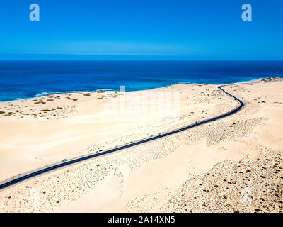 Antenna vista sopra di giallo spiaggia sabbiosa tropicale con nero lunga strada e la vettura viaggia - blu oceano onde e Riva - tramonto con lunghi beaut Foto Stock