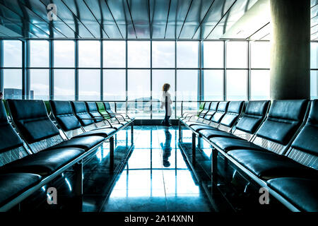 Giovane donna tourist gente camminare all'aeroporto specchiata sul pavimento pulito e guardando fuori dalla finestra per il filghts start e arrivare - un ritardo Foto Stock