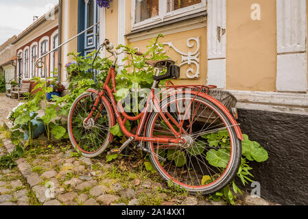 Un rosso retrò bike su una pavimentazione di ciottoli, appoggiato contro una parete con hollyhochs, AErøskøbing, Danimarca, luglio 13, 2019 Foto Stock