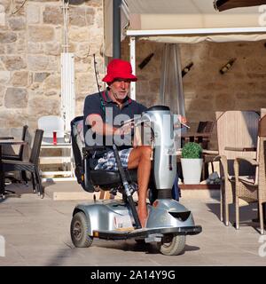 Ritratto di uomo anziano in sedia elettrica guida attraverso le strade di Primosten in Croazia Foto Stock