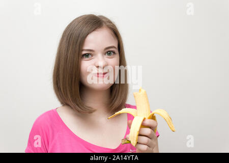 Ritratto di caucasici sorridente ragazza donna mangiare e masticare giallo banana in mano. Uno stile di vita sano, frutta dieta vegetariana. Foto Stock