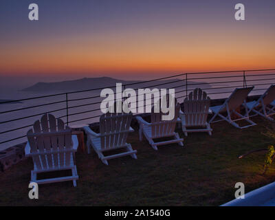 Vuoto sedie a sdraio sul balcone aperto con il maestoso paesaggio di foggy rocce e mare al tramonto in Grecia Santorini Foto Stock