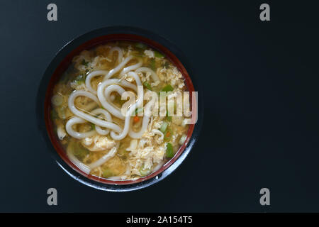 Vista superiore della zuppa giapponese con il tradizionale 'Udon' farina di grano a base di noodle in vaso in ceramica su sfondo nero Foto Stock