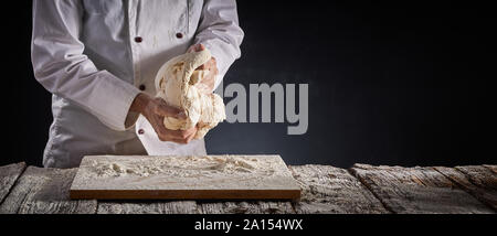 Baker dello chef impastare una grande porzione di impasto con le mani durante la preparazione su una infarinata scheda di legno in un panorama rustico banner con copia sp Foto Stock