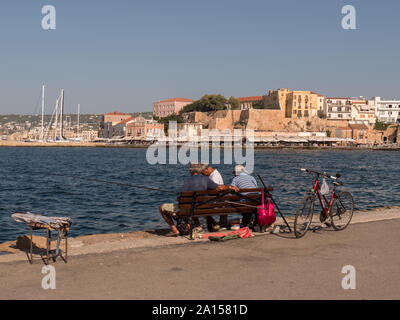 Tre persone sedute su una panchina nel porto di Chania, Creta Foto Stock