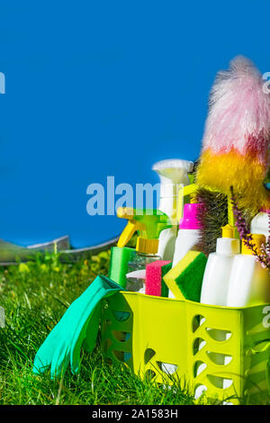 Un assortimento di bottiglie di plastica nel cestello di verde, con materiali per la pulizia insieme con spugne, spazzola sulla molla esterna sullo sfondo Foto Stock