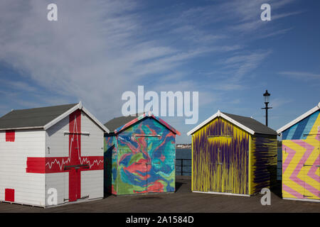 Quattro dipinte luminosamente capanne sulla spiaggia / getta sul molo di Southend, Essex. Foto Stock
