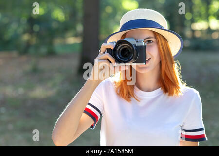 Bella ragazza con i capelli rossi di scattare una foto con la fotocamera in estate park. Foto Stock