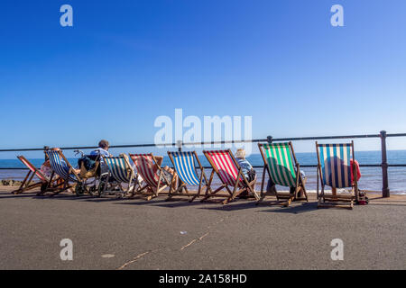 SIDMOUTH, Devon, Inghilterra - 20 settembre 2019: la gente seduta in sedie a sdraio che si affaccia sulla spiaggia verso il mare. Godendo l'ultimo del sole estivo. Foto Stock