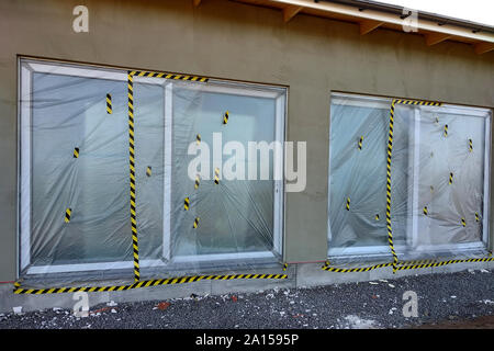 Le finestre di una casa in costruzione coperto con pellicola protettiva in plastica. Foto Stock