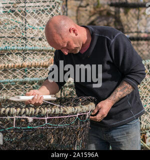 Un uomo che ripara una rete di aragosta a Kingswear, Devon, Regno Unito Foto Stock