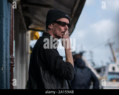 Un uomo in un beanie hat di fumare una sigaretta in piedi sulla strada Foto Stock