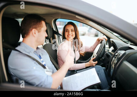 Maschio istruttore auto prende in esame giovane donna. Problema pratico. Allegro e felice studente positivo guardare al maestro e sorriso Foto Stock