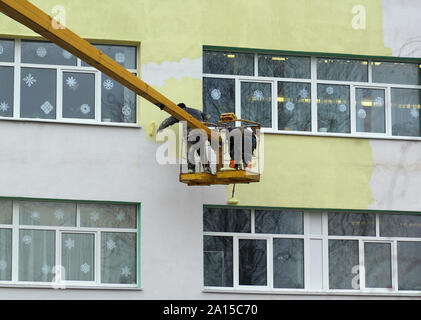 Mestiere pericoloso, pittori lavorando su gru mobile platform e vernice edificio multipiano giallo su un sordo a freddo giorno d'inverno. Foto Stock