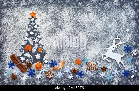 Albero di Natale fatto di farina su uno sfondo nero con i fiocchi di neve, cervi, anice stelle, i cookie e la cannella, farina bianca appare come la neve. Vista dall'alto. Foto Stock