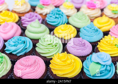 Tortini di cioccolato o coppa di torte con ghiaccio o la glassa, rosa, viola, blu, giallo e crema con foglie verdi, rose e decorazioni floreali Foto Stock