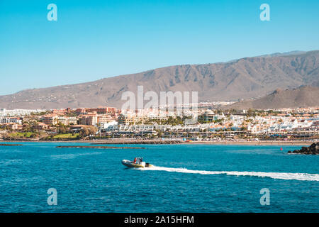 Imbarcazione a motore in costa dell'oceano con spiaggia e hotel in background, Tenerife Foto Stock