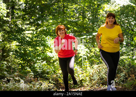 Due donne di mezza età che corre attraverso una foresta Foto Stock