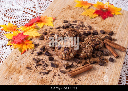 Biscotti al cioccolato su un tavolo di legno con bastoncini di cannella. In autunno il cibo stile foto con foglie Foto Stock