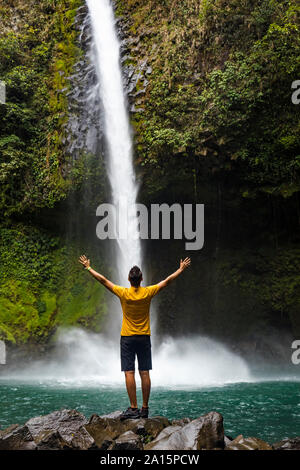 Viaggiatore con le braccia sollevate godendo La Fortuna cascata, La Fortuna, Costa Rica Foto Stock