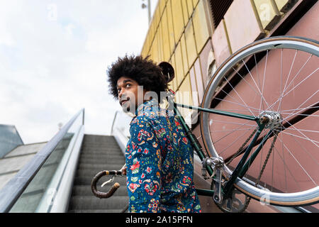 Elegante uomo che porta bicicletta su escalator Foto Stock