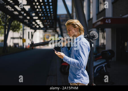 Giovane uomo con un telefono cellulare che trasportano e-scooter in città Foto Stock